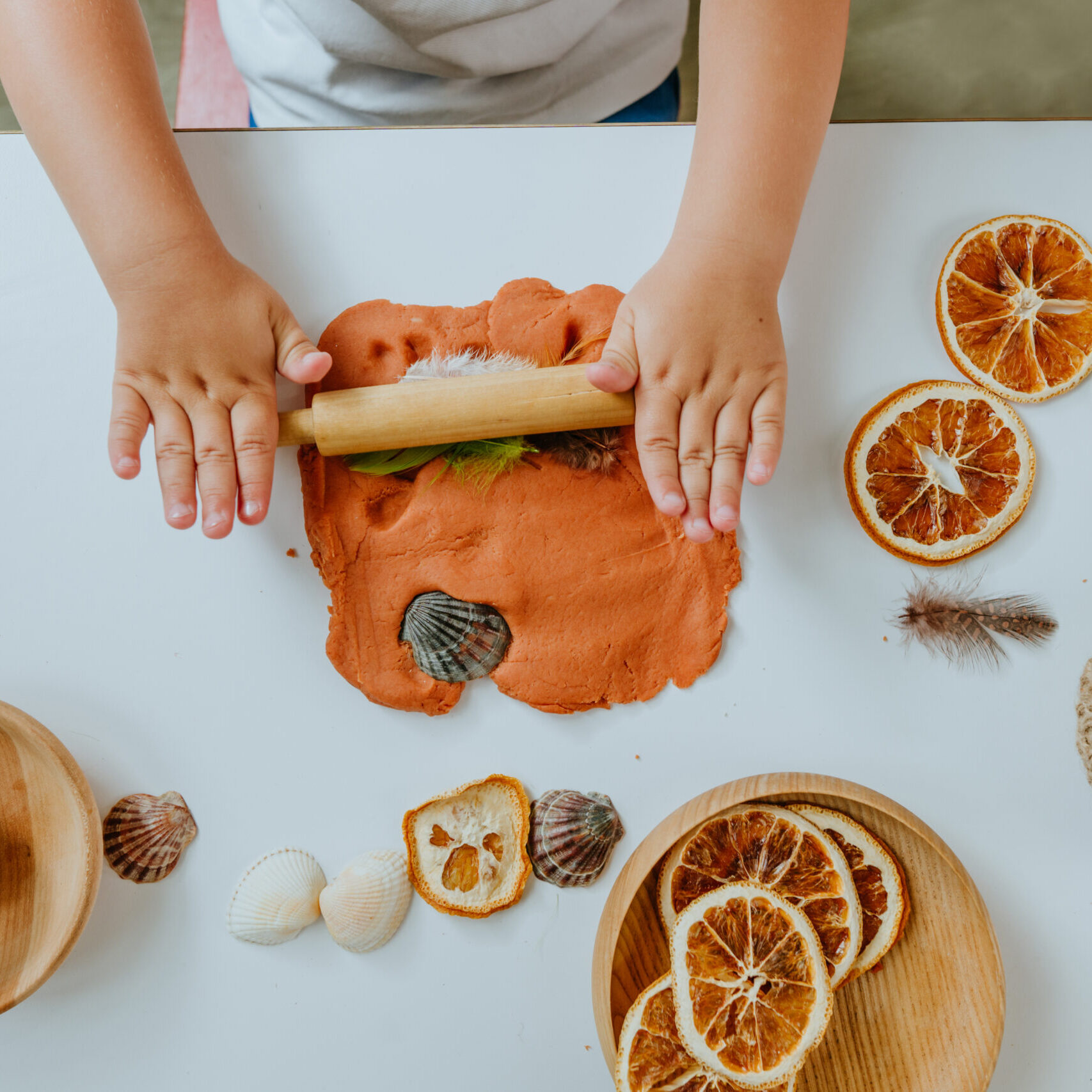 Child making prints on the dough using natural materials dry orange slices, cones, shells, feathers in kindergarten. Early development concept. Top view, flat lay.