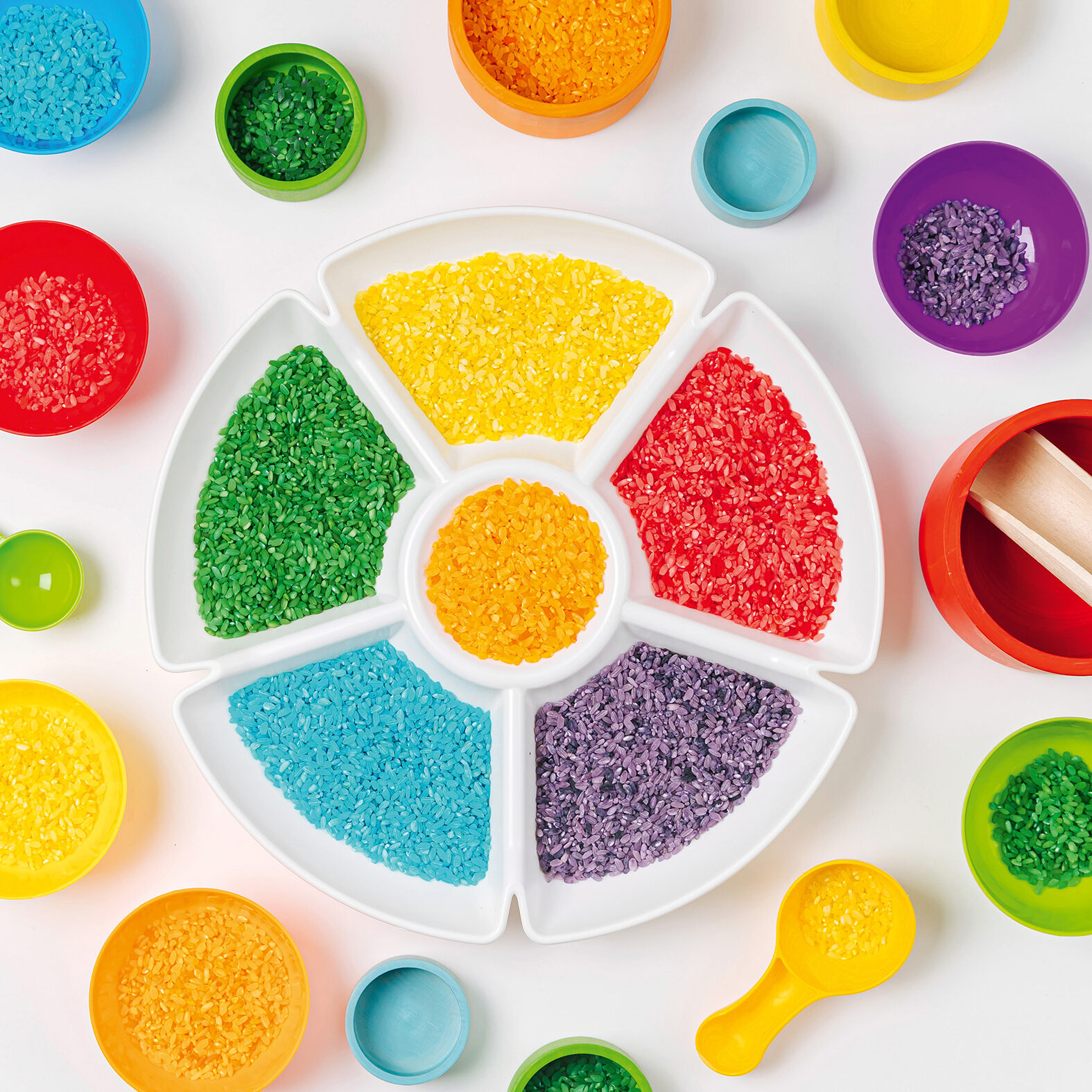 Play tray and bowls in rainbow colors with colored rice and scoops. Sensory bin toddler. Montessori material. Learning colors. Scooping and pouring activity for kids. Learning and development of child